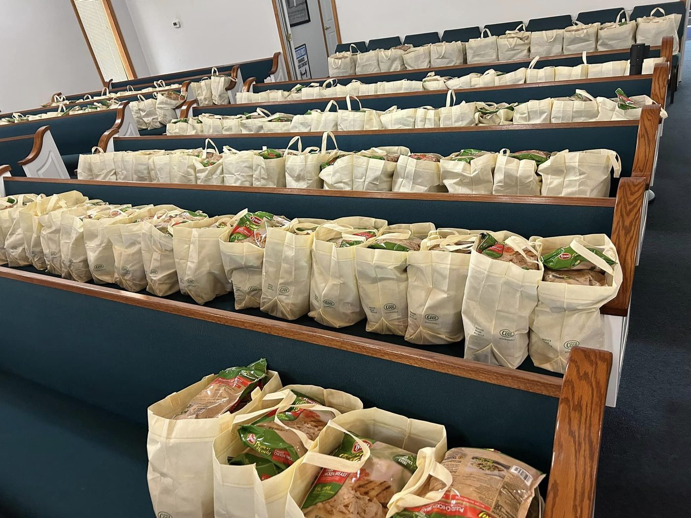 Hundreds of tote bags packed with food ready for distribution, lined up in the church pews
